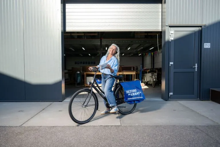 Content image krantenbezorgster op de fiets bij het depot